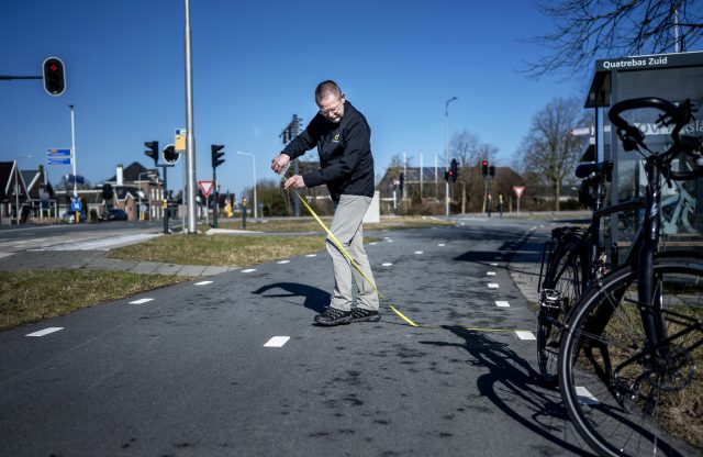 Vrijwilliger van de Fietsersbond staat met een meetlat op het fietspad en meet de breedte van het pad op.